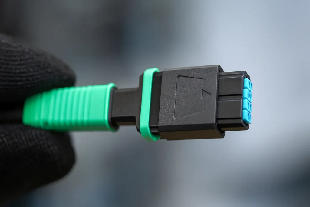 Gloved hand holding an MPO connector showing ferrules and keyed housing